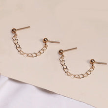 Load image into Gallery viewer, Pair of hypoallergenic surgical stainless steel double piercing earrings, featuring heart studs connected by a delicate chain, plated in gold
