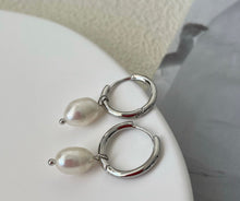 Load image into Gallery viewer, Huggie hoop earrings made of surgical stainless steel, featuring 6mm or 8mm freshwater pearls, showcasing a minimalist and elegant design.
